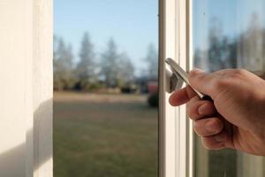 Hand opens a metal latch on the frame of a white wooden window, indoors. photo