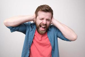 Caucasian man in stress, he is tired of the noise, covers ears with hands and shouts loudly. Psychological health concept. photo