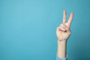 Victory sign, two fingers up, on a blue background. Copy space.