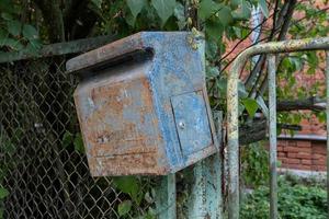 Mailbox is hanging on the fence. Old, rusty mailbox with peeling paint. photo