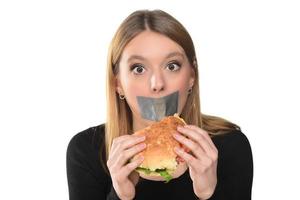 retrato de una hermosa joven divertida con cinta adhesiva sobre su boca en el fondo blanco, rubia sosteniendo una bandeja con hamburguesa foto