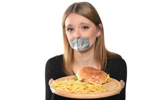 retrato de una hermosa joven divertida con cinta adhesiva sobre su boca en el fondo blanco, rubia sosteniendo una bandeja con hamburguesa foto