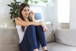 Unhappy young woman covering face with hands, crying alone close up, depressed girl sitting on couch at home, health problem or thinking about bad relationships, break up with boyfriend, divorce photo