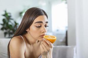 mujer enferma que intenta sentir el olor a media naranja fresca, tiene síntomas de covid-19, infección por el virus de la corona - pérdida del olfato y el gusto. uno de los principales signos de la enfermedad. foto