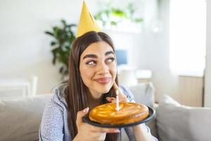 nuevo concepto normal. mujer feliz celebrando su cumpleaños sola. mujer joven sosteniendo un pastel. fiesta de cumpleaños en casa. videollamada familiar. distanciamiento social. vida en casa. foto