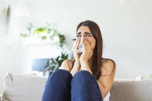 mujer joven infeliz cubriendo la cara con las manos, llorando sola de cerca, chica deprimida sentada en el sofá en casa, problema de salud o pensando en malas relaciones, romper con su novio, divorciarse foto