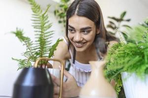 Woman caring for plants next to steam aroma oil diffuser on the table at home, steam from humidifier. Humidification of air in apartment during the period of self-isolation due to coronavirus pandemic photo