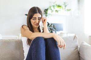 Unhappy young woman covering face with hands, crying alone close up, depressed girl sitting on couch at home, health problem or thinking about bad relationships, break up with boyfriend, divorce photo