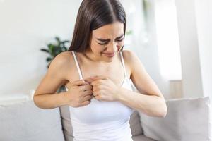 Woman sitting with strong chest pain and hands touching her chest while having trouble at home, Heart attack or heart failure symptom photo
