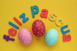 Feliz Pascua, Happy Easter letters on spanish and color eggs on yellow background. Holiday banner, flatlay creative composition. Greeting card, poster, banner, web. Top view festive concept. Flat lay photo