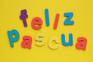 Feliz Pascua, Happy Easter on spanish colored lettering on yellow background. Holiday spring compostion concept. Creative idea for greeting card, poster, banner, invitation. Top view, flat lay photo