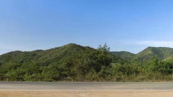 Horizontal view of asphalt road in Thailand. Background of green forest and mountain under the blue sky. photo