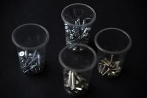 Construction bolts and screws in plastic cups on a black background. Construction accessories. photo