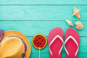 Beach holidays. Pink flip flops, summer hat with candy and copy space on blue wooden background. Top view. Mock up photo