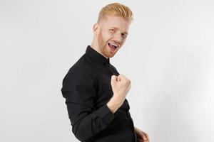 Reach the goal concept. Happy excited shock young guy entrepreneur isolated on gray background. Copy space. Close up Successful Redheaded man with red beard in stylish black shirt. Positive smart male photo