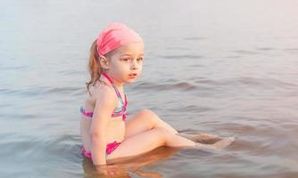 The child is bathing in the river. A little girl in a swimsuit on vacation in the summer. photo