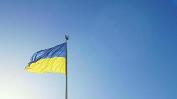 la bandera ucraniana de colores nacionales azul y amarillo en el asta de la bandera ondea en el viento contra el cielo azul y el sol naciente de la mañana. el símbolo oficial del estado de los ucranianos. patriotismo. video