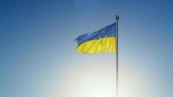 The Ukrainian flag of the national color on the flagpole is fluttering in the wind against the blue sky and the morning rising sun. The official state symbol of Ukrainians. Variable focus. video