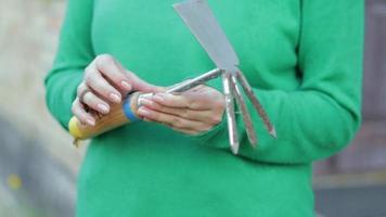 Kaukasisch vrouw tuinman in de tuin shows een hark. de concept van tuinieren en duurzame zomer. vrouw hand- met een tuin hulpmiddel. bijl hark voor tuinieren in vrouw handen. video