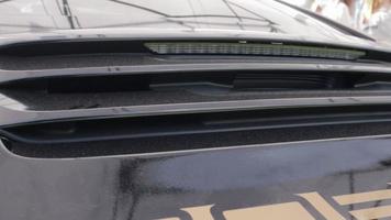 modelo de carro esportivo alemão brilhante 911 com tinta preta reflexiva. detalhes do spoiler traseiro ativo e lanternas traseiras. conceito de detalhamento do carro. close-up de um porta-malas com spoiler em uma concessionária de carros. video