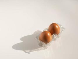 Two chicken eggs in a transparent plastic container on a white background. photo