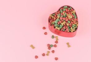 comida seca para perros en un tazón con forma de corazón rojo y sobre fondo rosa. concepto de amante de las mascotas y el día de san valentín. foto