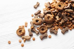 Dry food for dogs of different shapes on a white wooden background.