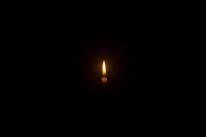 pequeña llama de vela encendida o luz que brilla en una vela blanca sobre fondo negro u oscuro en la mesa de la iglesia para Navidad, funeral o servicio conmemorativo con espacio para copiar foto