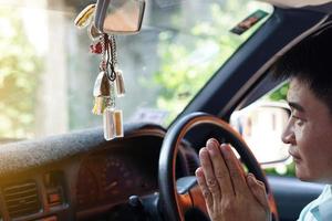 el conductor asiático está orando por una conducción segura y buena suerte de los amuletos tailandeses de buda en su automóvil. concepto, fe y creencia budista por santidad y suerte. prevención de accidentes. foto