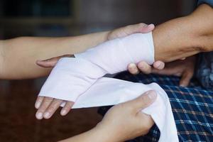 cierre las manos envolviendo la muñeca torcida del paciente con una venda elástica. concepto, primeros auxilios y tratamiento de lesiones en el brazo. accidente. seguro. foto