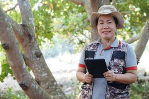 Asian woman botanist is in forest, hold smart tablet to survey and collect information of botanical plants by using smart tablet. Concept , adventure, field research about environment. photo