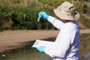 El investigador ambiental del hombre asiático sostiene un tubo de agua de muestra para inspeccionar desde el lago. concepto, exploración, análisis de la calidad del agua de fuente natural. investigación de campo en ecología. foto