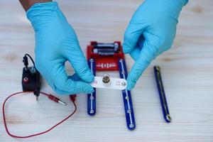 las manos de cerca usan guantes azules y sostienen un mini kit de bombillas para demostrar el experimento científico sobre el circuito eléctrico. concepto, herramienta científica para la educación, lección de laboratorio. aprender haciendo. foto