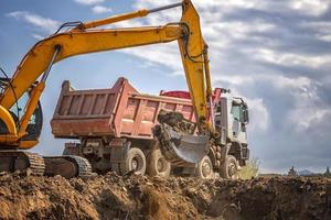 Yellow excavator and empty dump truck working at the construction site photo