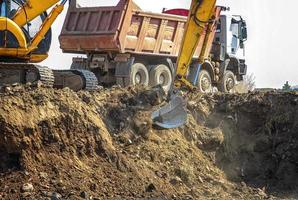 Excavator is loading excavation on the truck. Heavy construction equipment consisting of a boom, dipper or stick, bucket, and cab on a rotating platform. photo