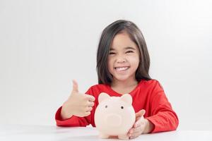 niña asiática ahorrando dinero en una alcancía, aprendiendo a ahorrar, los niños ahorran dinero para la educación futura. concepto de dinero, finanzas, seguros y personas foto