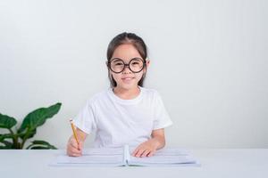 retrato de una pequeña alumna escribiendo en el escritorio en el estudio de una estudiante haciendo pruebas en la escuela primaria. niños escribiendo notas en el aula. concepto de conocimiento educativo foto