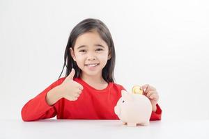 Little Asian girl saving money in a piggy bank, learning about saving, Kid save money for future education. Money, finances, insurance, and people concept photo