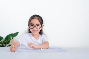 retrato de una pequeña alumna escribiendo en el escritorio en el estudio de una estudiante haciendo pruebas en la escuela primaria. niños escribiendo notas en el aula. concepto de conocimiento educativo foto