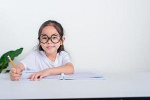 retrato de una pequeña alumna escribiendo en el escritorio en el estudio de una estudiante haciendo pruebas en la escuela primaria. niños escribiendo notas en el aula. concepto de conocimiento educativo foto