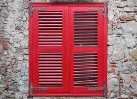 Red wooden blinds close the window on the old stone wall of the house. Old brick wall, idea for interior or loft studio and courtyard photo