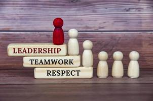 concepto de liderazgo: texto de liderazgo, trabajo en equipo y respeto sobre bloques de madera con figura de muñeca roja y blanca sobre fondo de cubierta de madera foto