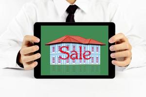 Businessman holding a tablet with house and red word sale photo