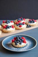 tartas variadas de frambuesa y arándanos sobre una mesa azul frente a un fondo gris. foto