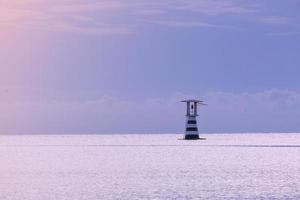 high lighthouse tower white and red color near sea shore port. construction building for navigator and signal safety. calm place for vacation sunrise photo