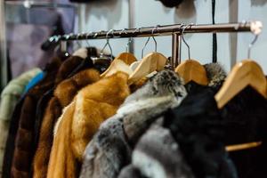un primer plano de un abrigo de piel natural de astracán de diferentes colores marrón, gris y negro, colgado en una fila en la tienda