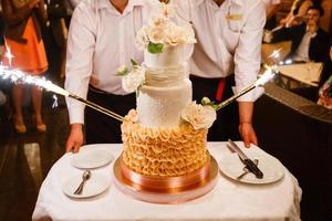 la novia y el novio felices cortan el pastel de bodas frente a los fuegos artificiales foto