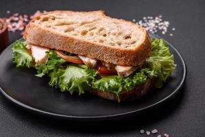 Fresh tasty sandwich with chicken, tomatoes and lettuce on a black plate photo