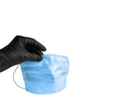una mano en un guante de goma sostiene una máscara respiratoria médica sobre fondo blanco. protección del médico contra virus covid-19 foto