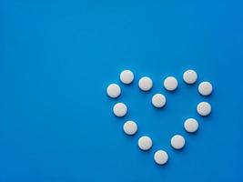 las tabletas de medicamentos se colocan en forma de corazón sobre un fondo azul. el concepto de tratamiento de enfermedades del corazón